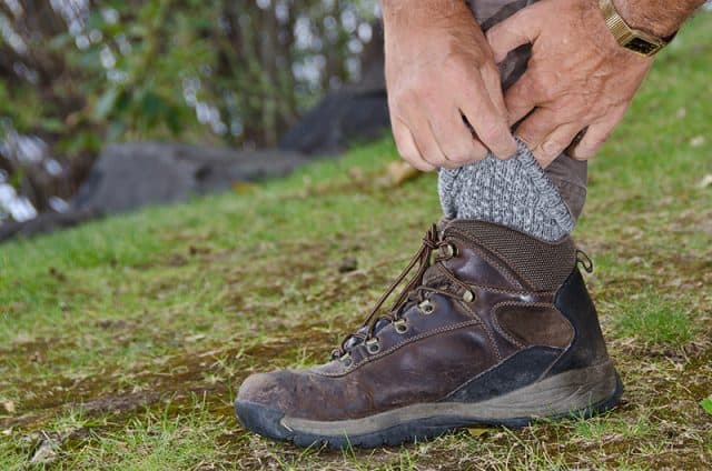A man on a hike pulling his socks over the bottom of his jeans.
