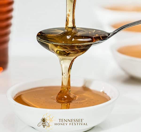 Honey being poured over a spoon that is waterfalling into a white cup with Tennessee Honey Festival at the bottom.