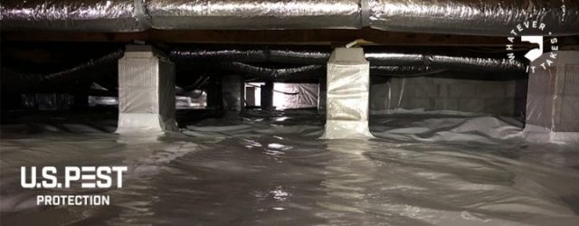 Underneath a home prepped with moisture barrier along the ground and beams of the home.