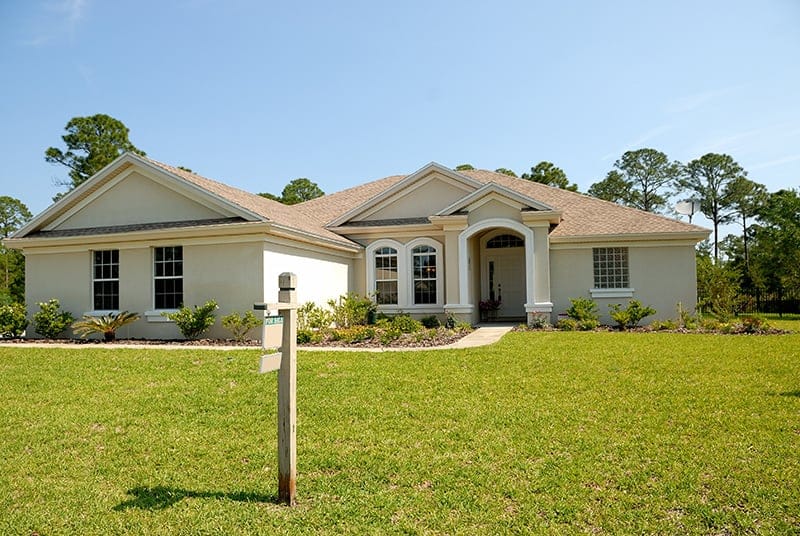 A beige house with a for sale sign in the front yard.