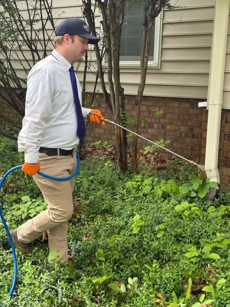 U.S. Pest Protection technician applying a spray treatment around the exterior perimeter of a home