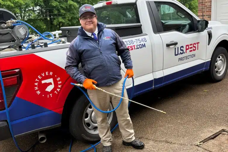 U.S. Pest Protection technician applying mosquito flea and tick barrier treatment to a residential yard