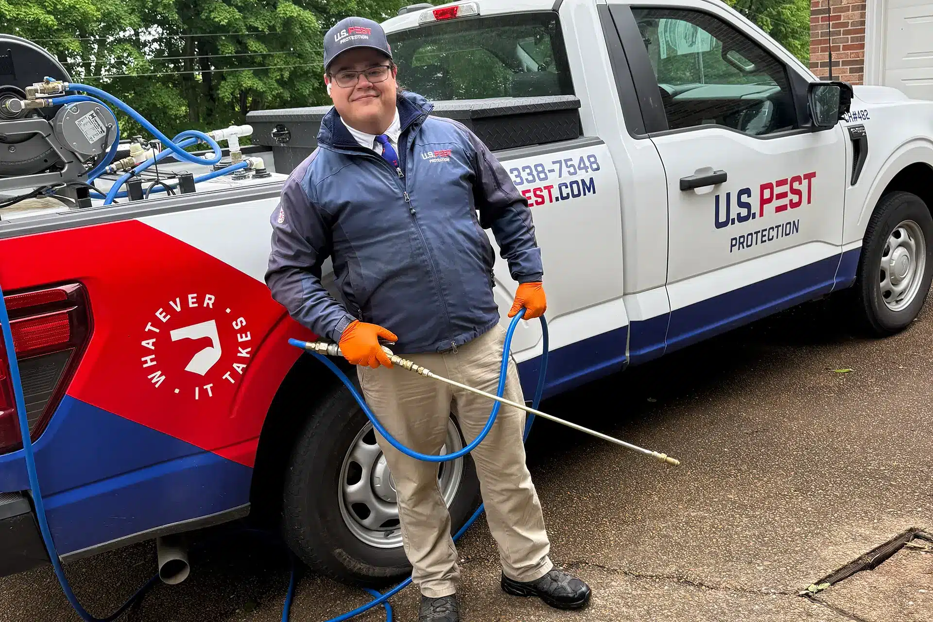 U.S. Pest Protection technician applying mosquito flea and tick barrier treatment to a residential yard